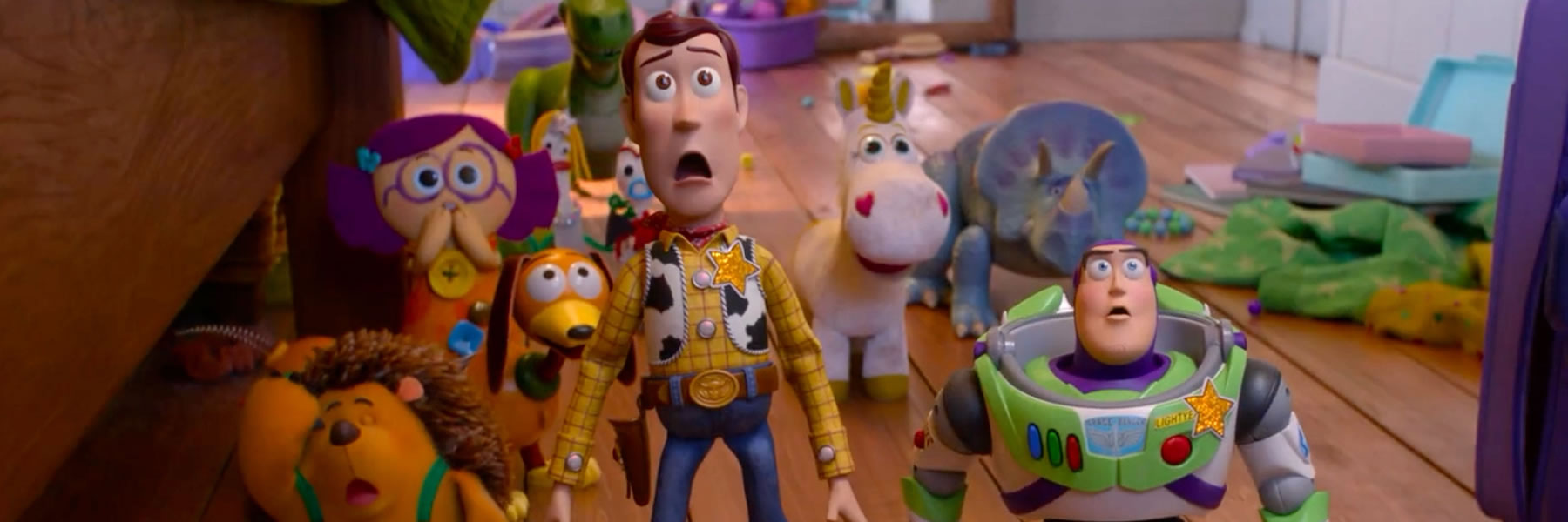 Group of toys including Woody and Buzz Lightyear standing in a cluttered child's playroom, all with surprised expressions.